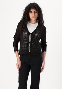 Melna adīta jaka ar V veida kakla izgriezumu, ar viļņotu apakšmalu un saišu aizdari, piedāvā atvērtu audumu rakstus un garām piedurknēm.