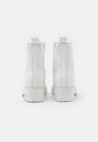 Bottines blanches en cuir, dotées d'une semelle épaisse blanche, d'une fermeture éclair et d'une languette à l'arrière. Surface texturée avec des détails de couture.