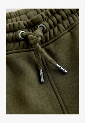Khaki Jogginghosen mit elastischem Bund, geflochtenem Kordelzug und metallischen Ösen. Glatte Stofftextur mit genähten Details.