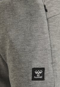 Grijze sportieve joggers van een zacht katoenen mix-stof, met een zijzak met rits en een zwart logo-opdracht met witte print.