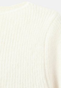 Tessuto a coste bianco sporco con una morbida e pelosa texture, che mostra la spalla e la parte superiore della manica di un indumento.