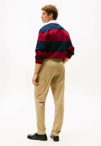 Suéter a rayas rojas y navy con un collar blanco, combinado con pantalones cargo de cintura elástica beige y zapatos negros. El look es relajado y casual.