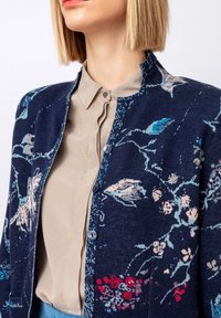 Jūras spēku džemperis ar ziedu rakstiem rozā un zilā krāsā, ar apaļu dekoltē, priekšējiem pogām un strukturētu adījuma materiālu.