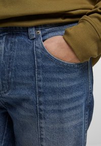 Jeans i denim i en lys blå vask med subtile falme. Har en frontlomme, metallknap-lukning og standard sømdetaljer.