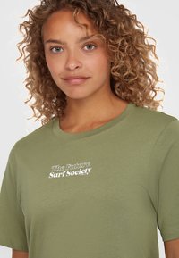 Oliivroheline T-särk pehmest kangast, ümmarguse kaelusega ja lühikeste varrukatega. Esitleb valget teksti "The Future Surf Society".