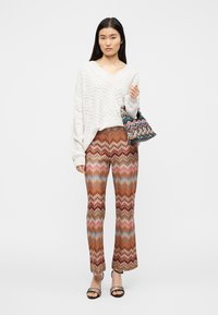 Λευκό πουλόβερ με υφή, V-λαιμόκοψη και άνετη εφαρμογή, συνδυασμένο με παντελόνια με σχέδιο, καμπάνα, σε ζεστούς τόνους καφέ, ροζ και μπλε.