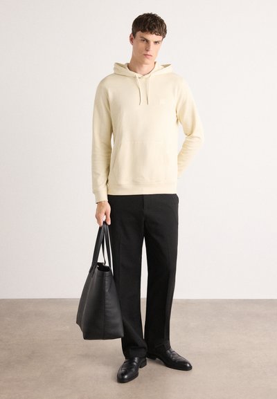 Haut à capuche jaune clair avec poche kangourou, associé à un pantalon noir et un sac en cuir noir. Tissu lisse, design simple et sans motifs.