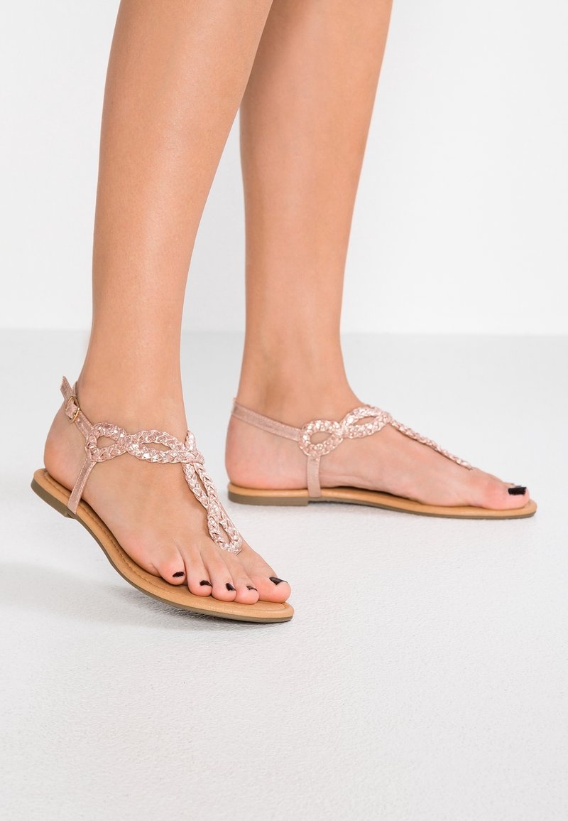 Litte sandaalit, joissa on vaaleanpunainen synteettinen päällinen, ja ne ovat punottu muotoilu ja varvaslenkki. Pohja on tan-värinen ja siinä on sileä pinta.