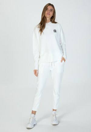 Weißes Sweatshirt mit rundem Halsausschnitt und schwarzem Logo auf der Brust, kombiniert mit weißen Jogginghosen mit Fronttaschen und schmalem Schnitt.