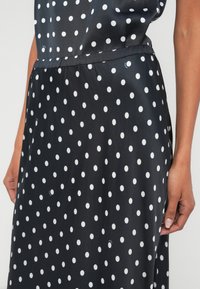 Črna obleka z belimi pikami, izdelana iz gladke tkanine. Ima elastični pas, dolžine do sredine meč in sproščen kroj.