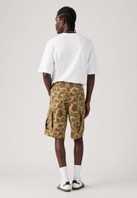 Green camo cargo shorts with multiple side pockets, paired with a loose-fitting white t-shirt and white socks, worn with black and white sneakers.