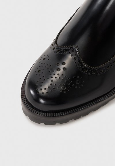 Black leather brogue shoe with perforated detailing, a smooth finish, and a textured sole. Features a scalloped edge around the ankle.
