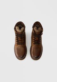 Brūnu ādas ziemas zābaku pāris ar vilnas oderi un tumši brūnām auklām, skatīti no augšas uz balta fona.