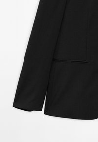 Zwarte blazer met een gestructureerde pasvorm, voorzien van een textuurstof, lange mouwen en een enkele borstzak. Strakke, moderne uitstraling.