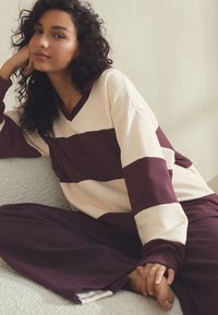 Langarmshirt met V-hals in roomwitte en bordeauxrode strepen, gecombineerd met bijpassende bordeauxrode broek, met een ontspannen pasvorm en zachte textuur.