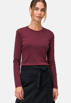 Haut long à manches bordeaux avec un col en vagues, en tissu doux et à coupe cintrée, assorti à une jupe noire taille haute avec une ceinture nouée.