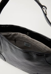 Borsa a spalla in pelle nera aperta per mostrare l'interno in tessuto beige con tasca con zip e etichetta "JOOP! JEANS".