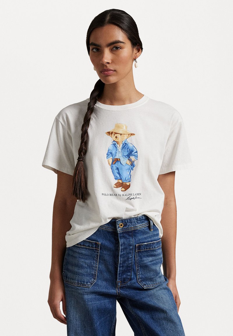 Tricou din bumbac alb cu un urs pictat îmbrăcat în haine din denim și o pălărie. Asortat cu blugi blue, punând în evidență un croi lejer și buzunare.