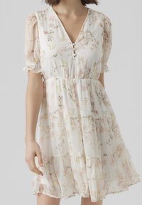 Robe blanche à fleurs avec manches courtes bouffantes, col en V et détails à boutons. Fabriquée en tissu léger avec un ourlet à volants et en couches, aux couleurs pastel.