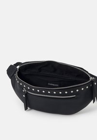 Sac banane en cuir noir avec fermeture éclair argentée et détails cloutés, ouvert pour montrer la doublure intérieure et une petite poche zippée à l'intérieur.