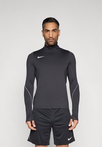 Μαύρο αθλητικό μπλουζάκι με μακριά μανίκια και ψηλό γιακά, με λευκές λεπτομέρειες στα πλευρά και φερμουάρ εμπρός. Συνδυάζεται με μαύρο σορτς που φέρει λογότυπο.