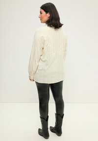 Camicia a maniche lunghe color beige chiaro con cuciture verticali colorate, leggings in ecopelle nera e stivali da cowboy neri. Taglio semplice e rilassato.