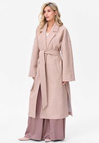 Długi, jasnoróżowy płaszcz wełniany z szerokimi rękawami, paskiem w talii i bocznymi rozcięciami, zestawiony z luźnymi satynowymi spodniami w dopasowanym odcieniu.
