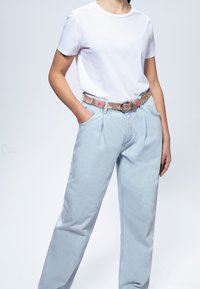 T-shirt blanc associé à un jean taille haute bleu clair et une ceinture à motifs avec des designs floraux et une boucle ronde.