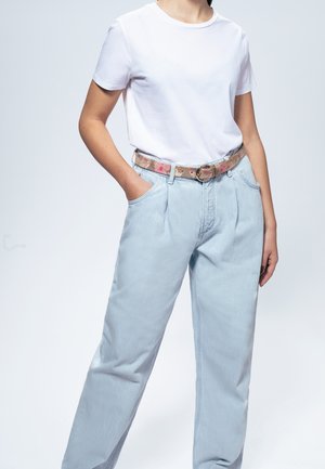 Witte t-shirt gecombineerd met lichtblauwe, high-waisted jeans en een patterned riem met bloemenpatronen en een ronde gesp.