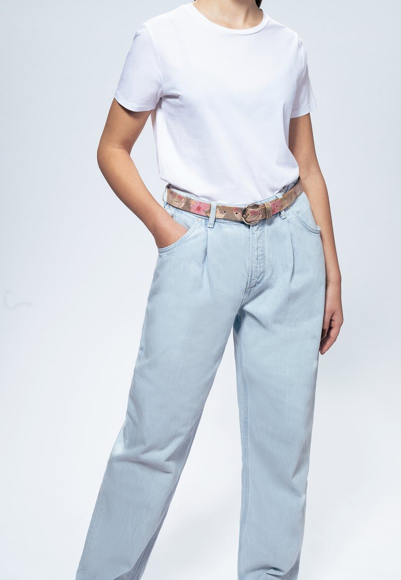T-shirt blanc associé à un jean taille haute bleu clair et une ceinture à motifs avec des designs floraux et une boucle ronde.