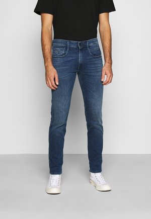 Blå denimjeans med slim passform, femfickorsdesign och blekt tvätt, kombinerat med vita sneakers och en svart t-shirt.