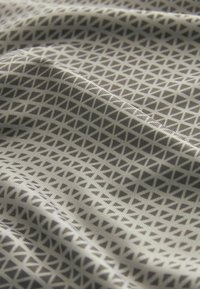 Tissu doux avec un motif répétitif de petits triangles gris foncé sur un fond gris clair avec des plis doux créant des ombres.