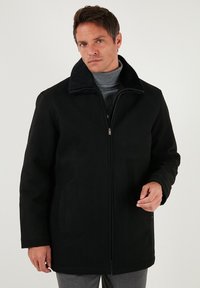 Melnas ziemas mētelis ar mīkstu, pūkainu apkakli, ar rāvējslēdzēju priekšpusē un sānu kabatām. Veidots ar strukturētu piegriezumu un gludu tekstūru.