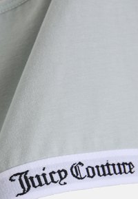 Svetlomodrá tkanina s hladkým povrchom má biely pás so značkou "Juicy Couture" v čiernom písme pozdĺž spodného okraja.