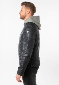 Schwarze Lederjacke mit grauem Kapuzen, taillierte Passform, mit Reißverschlusstaschen und Schulterakzenten. Glatte Textur mit einer eleganten Erscheinung.
