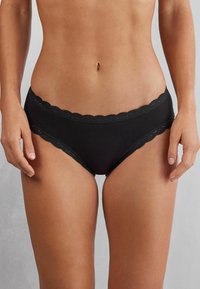 Zwarte onderbroek met kantafwerking en gegolfde rand, gemaakt van een gladde stof en met een stringmodel, geschikt voor dagelijks gebruik.