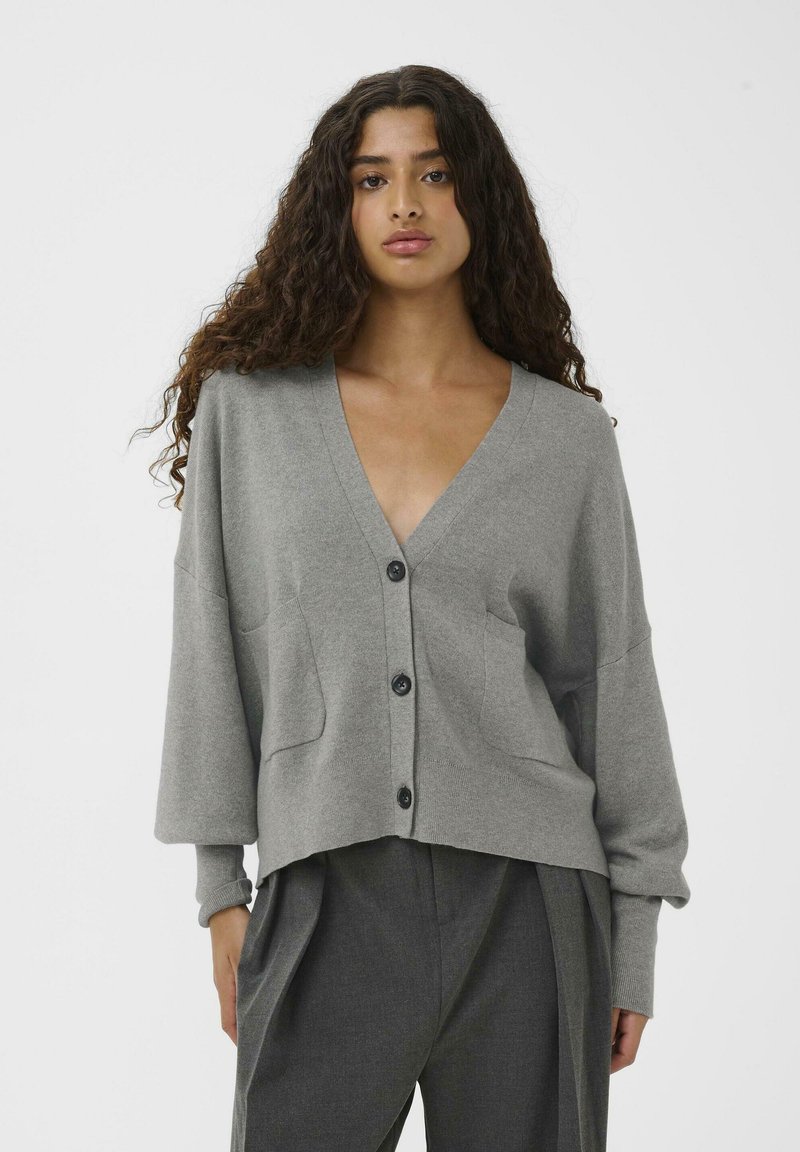Grå stickad cardigan med V-hals, sänkta axlar, två framfickor och mörka knappar. Tyget verkar mjukt med en slät textur.