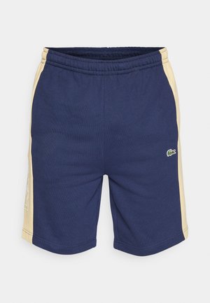 Pantalones cortos deportivos azul marino con acentos laterales amarillos, cinturilla elástica y detalles de logo bordado en verde. Confeccionados en un tejido suave y flexible.