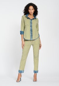 Green denim jacket with a blue denim collar, paired with matching green jeans, featuring rolled cuffs and stitching details.