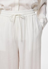 Pantalons en lin légers et blancs, dotés d'une taille élastique, d'un cordon de serrage, et de poches latérales, affichant une coupe décontractée et une texture lisse.