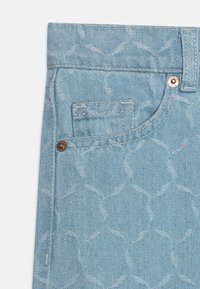 Svetlo modra jeans tkanina z nizko vidnim kro�žnim vzorcem. Majhna sprednja žepka z naglasom iz bronastega gumba je vidna.
