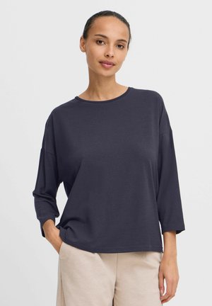 Donker marineblauwe langemouwen shirt met een ronde hals en een losse pasvorm. Zachte stof, relaxte mouwen en zichtbare stiksels. Gecombineerd met lichte broek.