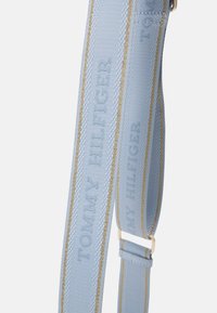 Cinghia in tessuto blu con logo "TOMMY HILFIGER" stampato in rilievo, accentuata da cuciture e hardware dorati. Lunghezza regolabile con una texture liscia.