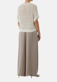 Otwarte dzianinowe beżowe top z krótkimi rękawami zestawione z wysokim stanem, szerokimi spodniami w kolorze taupe. Gładka tekstura materiału i luźny fason.