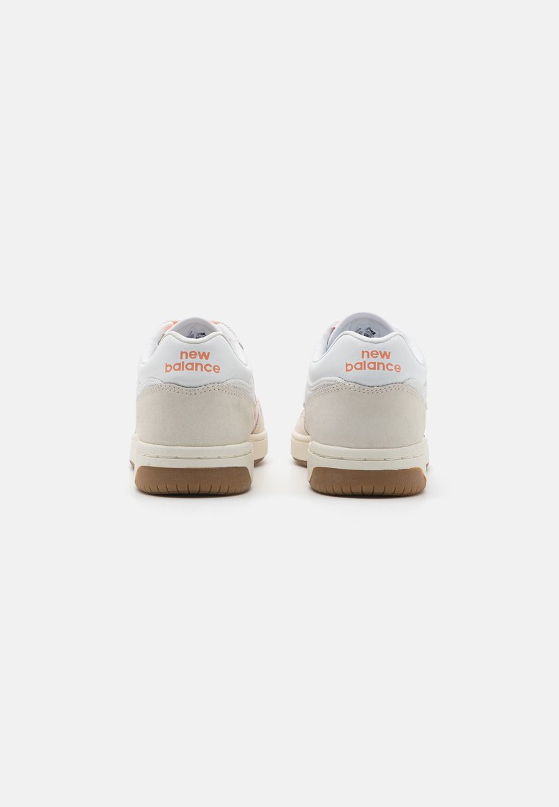 Baskets blanches avec des accents roses, présentant une partie en suède texturé, une semelle en caoutchouc et la marque "New Balance" sur le talon.