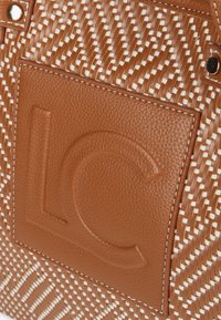 Brown woven handbag featuring a smooth leather patch embossed with "LC," contrasting white stitching along design lines.