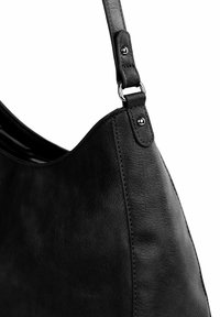 Černá kožená kabelka s hladkým povrchem, zakřiveného tvaru a odnímatelným popruhem uchyceným kovovými prvky.