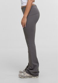 Pantalons de yoga gris ajustés avec une large ceinture et une texture lisse, fuselés au niveau de la cheville, associés à des chaussures de sport beiges.