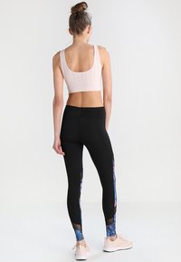 Podprsenka na sporty s výplní v jasně růžové barvě s perforovanými detaily, spárovaná s černými legínami s květinovými akcenty a síťovinovými panely po stranách.