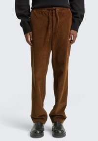 Bruine corduroy broek met een relaxte pasvorm, voorzien van een elastische tailleband, trekkoordsluiting en verticale ribbeltextuur.